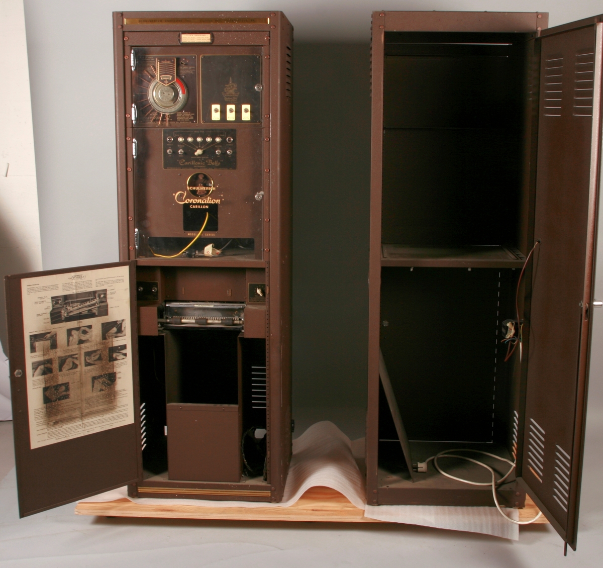 To brunmalte skap i metall (samme størrelse). Flere ventilasjonsrister.

Det ene skapet (A) inneholder avspiller, forsterker, klokkemekanikk, liten høytaler og øvrig elektronikk (noen deler ser ut å mangle). 
Øvre halvdel: bak pleksiglass som kan lukkes er styresentralen med instillinger for ulike klokkeprogrammer:
Til høyre er switch-knapper for å aktivere de tre funksjonene 
a) avspilling av musikkrull 
b) bruk av manuelt spillebord og 
c) timeslag.

Over til venstre er en timer for å skjemalegge de ulike aktivitetene:
1) Hverdag avspilling musikkrull
2) Søndag avspilling musikkrull
3) Hverdag avspilling timeslag
4) Søndag avspilling timeslag
5) Hverdag avspilling manuelt spillebord
6) Søndag avspilling manuelt spillebord

I tillegg er et eget panel for å velge ulike fomer av klokkeringinger ('BELL PEAL').

Nedre halvdel: Musikkrullmekanikk med en mekanisk avleser for musikkrullene ('tracker bar'). 30 spor; én for én tone hver. Papirullen løper over en rekke fjærbelastede(?) L-formet tangenter, en for hvert spor. Når et hull passerer en tangent løftes tangenten oppover og gir i sin tur et signal videre om å aktivere akkurat denne tonen.

Det andre skapet (B) idag tomt, usikker funksjon. Har strømforsyning. Sannsynlig forsterker for bruk av høytalere (C-F) i klokketårnet. Se elektronikk (H). Muligens også oppbevaring av musikkruller med mer.