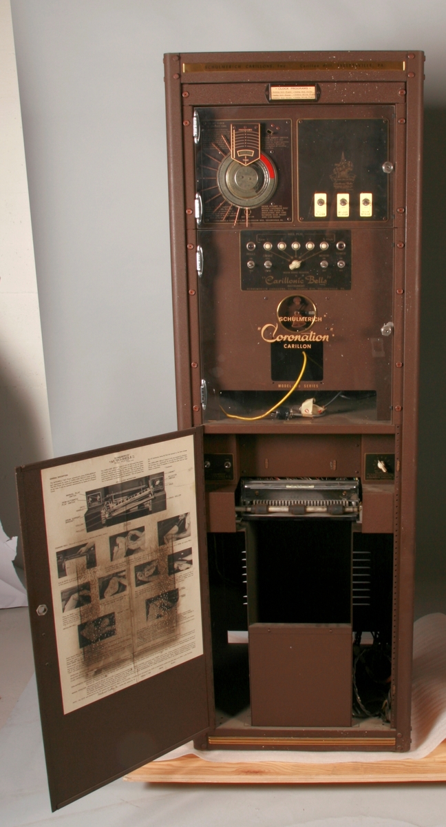 To brunmalte skap i metall (samme størrelse). Flere ventilasjonsrister.

Det ene skapet (A) inneholder avspiller, forsterker, klokkemekanikk, liten høytaler og øvrig elektronikk (noen deler ser ut å mangle). 
Øvre halvdel: bak pleksiglass som kan lukkes er styresentralen med instillinger for ulike klokkeprogrammer:
Til høyre er switch-knapper for å aktivere de tre funksjonene 
a) avspilling av musikkrull 
b) bruk av manuelt spillebord og 
c) timeslag.

Over til venstre er en timer for å skjemalegge de ulike aktivitetene:
1) Hverdag avspilling musikkrull
2) Søndag avspilling musikkrull
3) Hverdag avspilling timeslag
4) Søndag avspilling timeslag
5) Hverdag avspilling manuelt spillebord
6) Søndag avspilling manuelt spillebord

I tillegg er et eget panel for å velge ulike fomer av klokkeringinger ('BELL PEAL').

Nedre halvdel: Musikkrullmekanikk med en mekanisk avleser for musikkrullene ('tracker bar'). 30 spor; én for én tone hver. Papirullen løper over en rekke fjærbelastede(?) L-formet tangenter, en for hvert spor. Når et hull passerer en tangent løftes tangenten oppover og gir i sin tur et signal videre om å aktivere akkurat denne tonen.

Det andre skapet (B) idag tomt, usikker funksjon. Har strømforsyning. Sannsynlig forsterker for bruk av høytalere (C-F) i klokketårnet. Se elektronikk (H). Muligens også oppbevaring av musikkruller med mer.