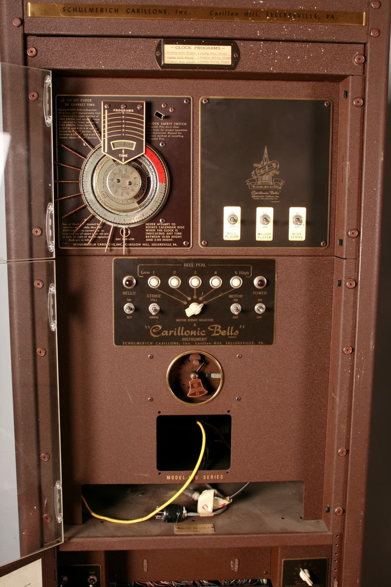 To brunmalte skap i metall (samme størrelse). Flere ventilasjonsrister.

Det ene skapet (A) inneholder avspiller, forsterker, klokkemekanikk, liten høytaler og øvrig elektronikk (noen deler ser ut å mangle). 
Øvre halvdel: bak pleksiglass som kan lukkes er styresentralen med instillinger for ulike klokkeprogrammer:
Til høyre er switch-knapper for å aktivere de tre funksjonene 
a) avspilling av musikkrull 
b) bruk av manuelt spillebord og 
c) timeslag.

Over til venstre er en timer for å skjemalegge de ulike aktivitetene:
1) Hverdag avspilling musikkrull
2) Søndag avspilling musikkrull
3) Hverdag avspilling timeslag
4) Søndag avspilling timeslag
5) Hverdag avspilling manuelt spillebord
6) Søndag avspilling manuelt spillebord

I tillegg er et eget panel for å velge ulike fomer av klokkeringinger ('BELL PEAL').

Nedre halvdel: Musikkrullmekanikk med en mekanisk avleser for musikkrullene ('tracker bar'). 30 spor; én for én tone hver. Papirullen løper over en rekke fjærbelastede(?) L-formet tangenter, en for hvert spor. Når et hull passerer en tangent løftes tangenten oppover og gir i sin tur et signal videre om å aktivere akkurat denne tonen.

Det andre skapet (B) idag tomt, usikker funksjon. Har strømforsyning. Sannsynlig forsterker for bruk av høytalere (C-F) i klokketårnet. Se elektronikk (H). Muligens også oppbevaring av musikkruller med mer.