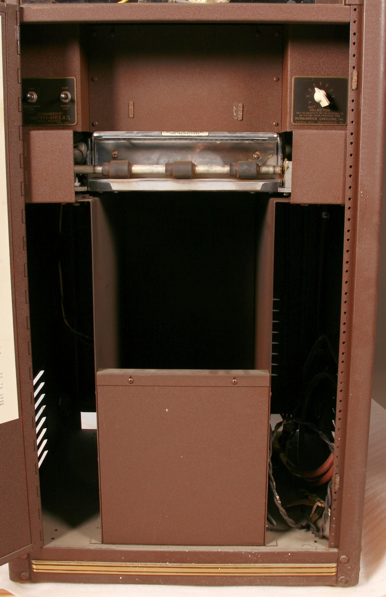 To brunmalte skap i metall (samme størrelse). Flere ventilasjonsrister.

Det ene skapet (A) inneholder avspiller, forsterker, klokkemekanikk, liten høytaler og øvrig elektronikk (noen deler ser ut å mangle). 
Øvre halvdel: bak pleksiglass som kan lukkes er styresentralen med instillinger for ulike klokkeprogrammer:
Til høyre er switch-knapper for å aktivere de tre funksjonene 
a) avspilling av musikkrull 
b) bruk av manuelt spillebord og 
c) timeslag.

Over til venstre er en timer for å skjemalegge de ulike aktivitetene:
1) Hverdag avspilling musikkrull
2) Søndag avspilling musikkrull
3) Hverdag avspilling timeslag
4) Søndag avspilling timeslag
5) Hverdag avspilling manuelt spillebord
6) Søndag avspilling manuelt spillebord

I tillegg er et eget panel for å velge ulike fomer av klokkeringinger ('BELL PEAL').

Nedre halvdel: Musikkrullmekanikk med en mekanisk avleser for musikkrullene ('tracker bar'). 30 spor; én for én tone hver. Papirullen løper over en rekke fjærbelastede(?) L-formet tangenter, en for hvert spor. Når et hull passerer en tangent løftes tangenten oppover og gir i sin tur et signal videre om å aktivere akkurat denne tonen.

Det andre skapet (B) idag tomt, usikker funksjon. Har strømforsyning. Sannsynlig forsterker for bruk av høytalere (C-F) i klokketårnet. Se elektronikk (H). Muligens også oppbevaring av musikkruller med mer.