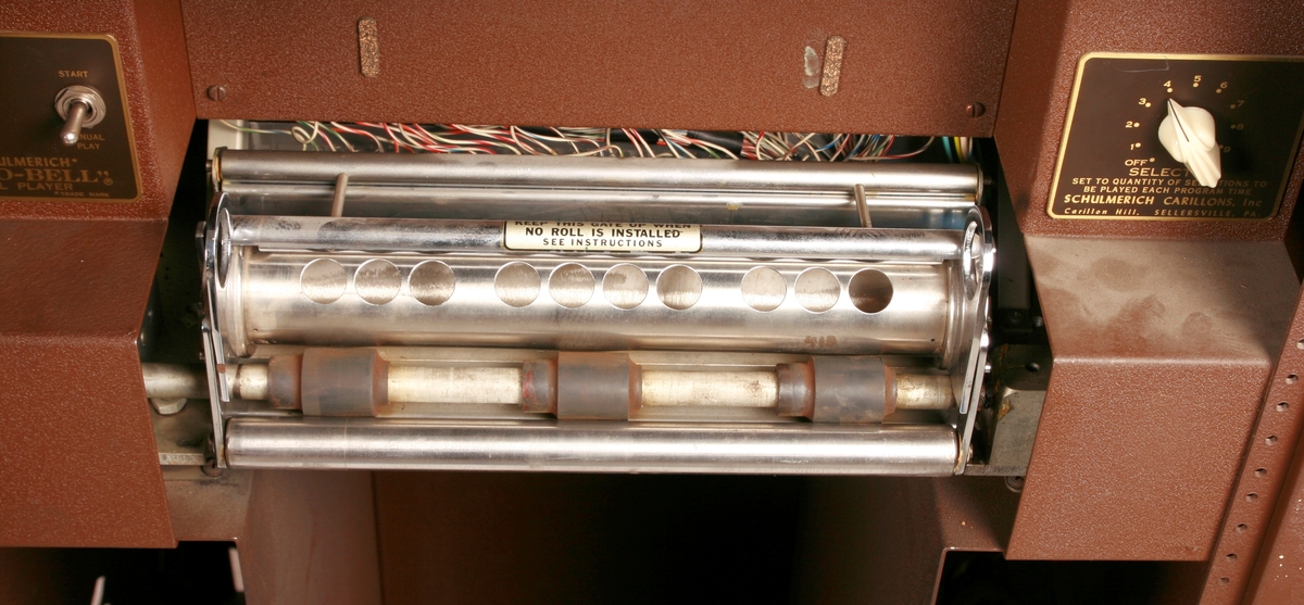 To brunmalte skap i metall (samme størrelse). Flere ventilasjonsrister.

Det ene skapet (A) inneholder avspiller, forsterker, klokkemekanikk, liten høytaler og øvrig elektronikk (noen deler ser ut å mangle). 
Øvre halvdel: bak pleksiglass som kan lukkes er styresentralen med instillinger for ulike klokkeprogrammer:
Til høyre er switch-knapper for å aktivere de tre funksjonene 
a) avspilling av musikkrull 
b) bruk av manuelt spillebord og 
c) timeslag.

Over til venstre er en timer for å skjemalegge de ulike aktivitetene:
1) Hverdag avspilling musikkrull
2) Søndag avspilling musikkrull
3) Hverdag avspilling timeslag
4) Søndag avspilling timeslag
5) Hverdag avspilling manuelt spillebord
6) Søndag avspilling manuelt spillebord

I tillegg er et eget panel for å velge ulike fomer av klokkeringinger ('BELL PEAL').

Nedre halvdel: Musikkrullmekanikk med en mekanisk avleser for musikkrullene ('tracker bar'). 30 spor; én for én tone hver. Papirullen løper over en rekke fjærbelastede(?) L-formet tangenter, en for hvert spor. Når et hull passerer en tangent løftes tangenten oppover og gir i sin tur et signal videre om å aktivere akkurat denne tonen.

Det andre skapet (B) idag tomt, usikker funksjon. Har strømforsyning. Sannsynlig forsterker for bruk av høytalere (C-F) i klokketårnet. Se elektronikk (H). Muligens også oppbevaring av musikkruller med mer.