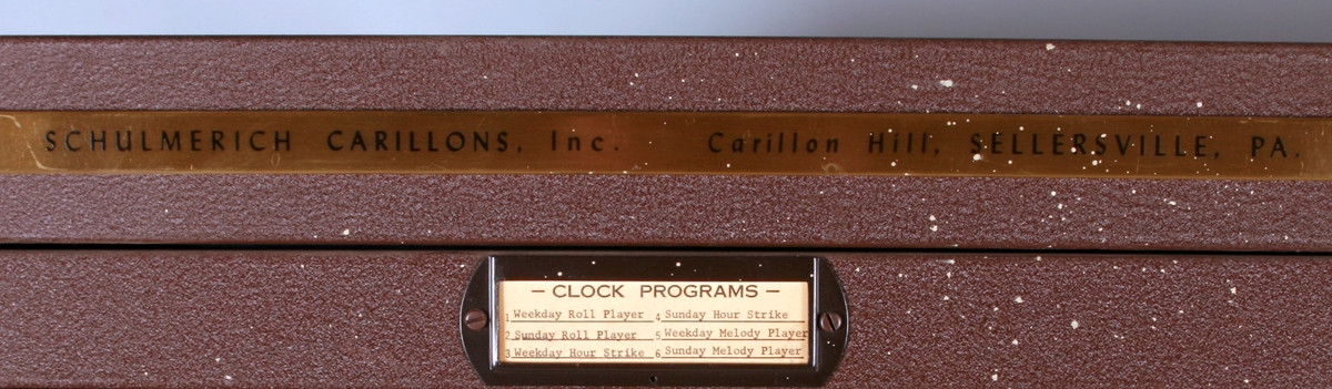 To brunmalte skap i metall (samme størrelse). Flere ventilasjonsrister.

Det ene skapet (A) inneholder avspiller, forsterker, klokkemekanikk, liten høytaler og øvrig elektronikk (noen deler ser ut å mangle). 
Øvre halvdel: bak pleksiglass som kan lukkes er styresentralen med instillinger for ulike klokkeprogrammer:
Til høyre er switch-knapper for å aktivere de tre funksjonene 
a) avspilling av musikkrull 
b) bruk av manuelt spillebord og 
c) timeslag.

Over til venstre er en timer for å skjemalegge de ulike aktivitetene:
1) Hverdag avspilling musikkrull
2) Søndag avspilling musikkrull
3) Hverdag avspilling timeslag
4) Søndag avspilling timeslag
5) Hverdag avspilling manuelt spillebord
6) Søndag avspilling manuelt spillebord

I tillegg er et eget panel for å velge ulike fomer av klokkeringinger ('BELL PEAL').

Nedre halvdel: Musikkrullmekanikk med en mekanisk avleser for musikkrullene ('tracker bar'). 30 spor; én for én tone hver. Papirullen løper over en rekke fjærbelastede(?) L-formet tangenter, en for hvert spor. Når et hull passerer en tangent løftes tangenten oppover og gir i sin tur et signal videre om å aktivere akkurat denne tonen.

Det andre skapet (B) idag tomt, usikker funksjon. Har strømforsyning. Sannsynlig forsterker for bruk av høytalere (C-F) i klokketårnet. Se elektronikk (H). Muligens også oppbevaring av musikkruller med mer.