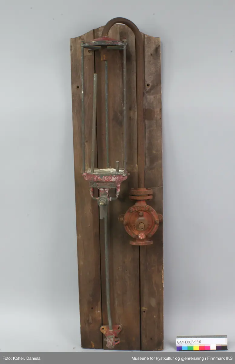 Bensinpumpa består av metall og har forskjellige ventiler. Den er festet til ei bakplate bestående av 3 planker som er avrundet oppe. På baksida er platen stabilisert med tverrgående bord oppe, nede og i midten. Pumpens glassbeholder er knust og fjernet. 