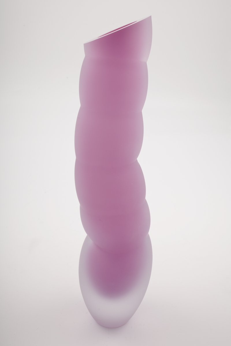 Vase i underfangsglass. Et sjikt i opakt lillafarget glass innerst, deretter et tykt sjikt i klart glass. Flerleddet kuleformet korpus, hvis ytterside er mattet ved hjelp av sandblåsing. Vasens sirkulære munning er planslipt.