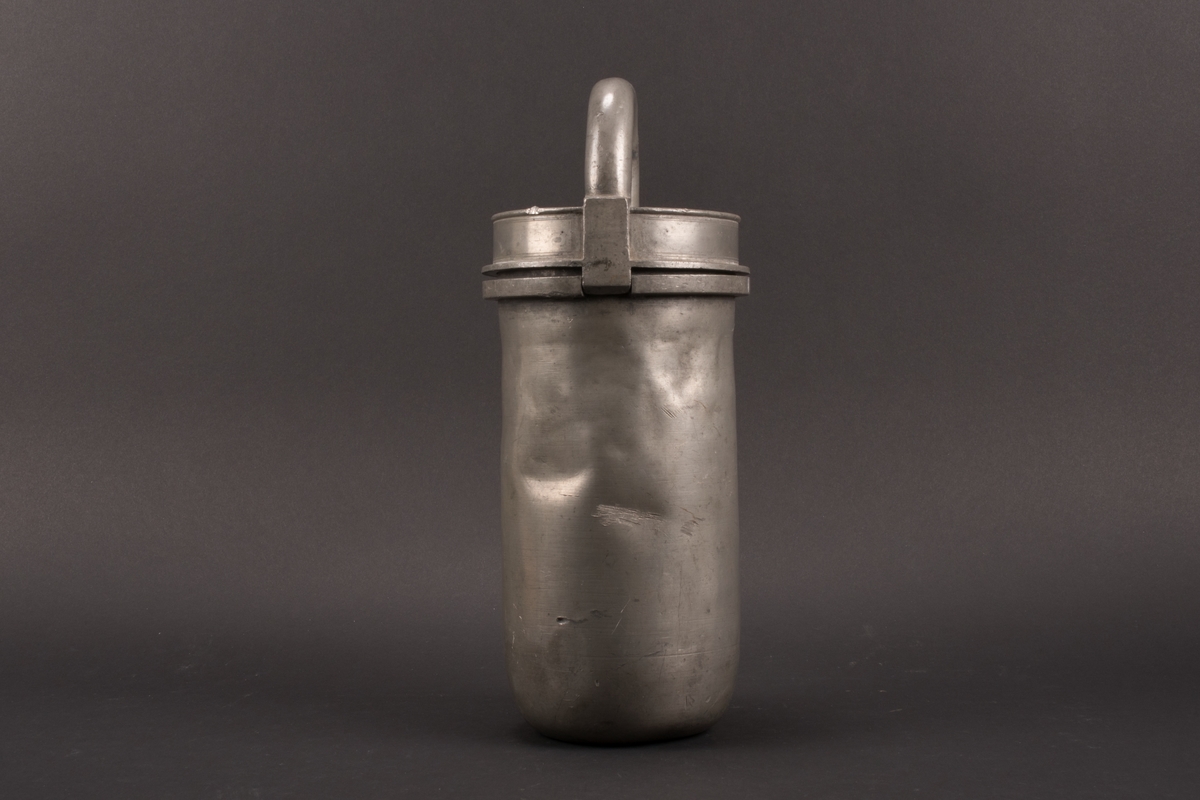 Cylindrisk glassform av tenn. Lock med halvcirkelformat handtag. Formens botten är något rundad.