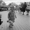 Danslek med barn och vuxna. Skansen. Liten flicka ser på.