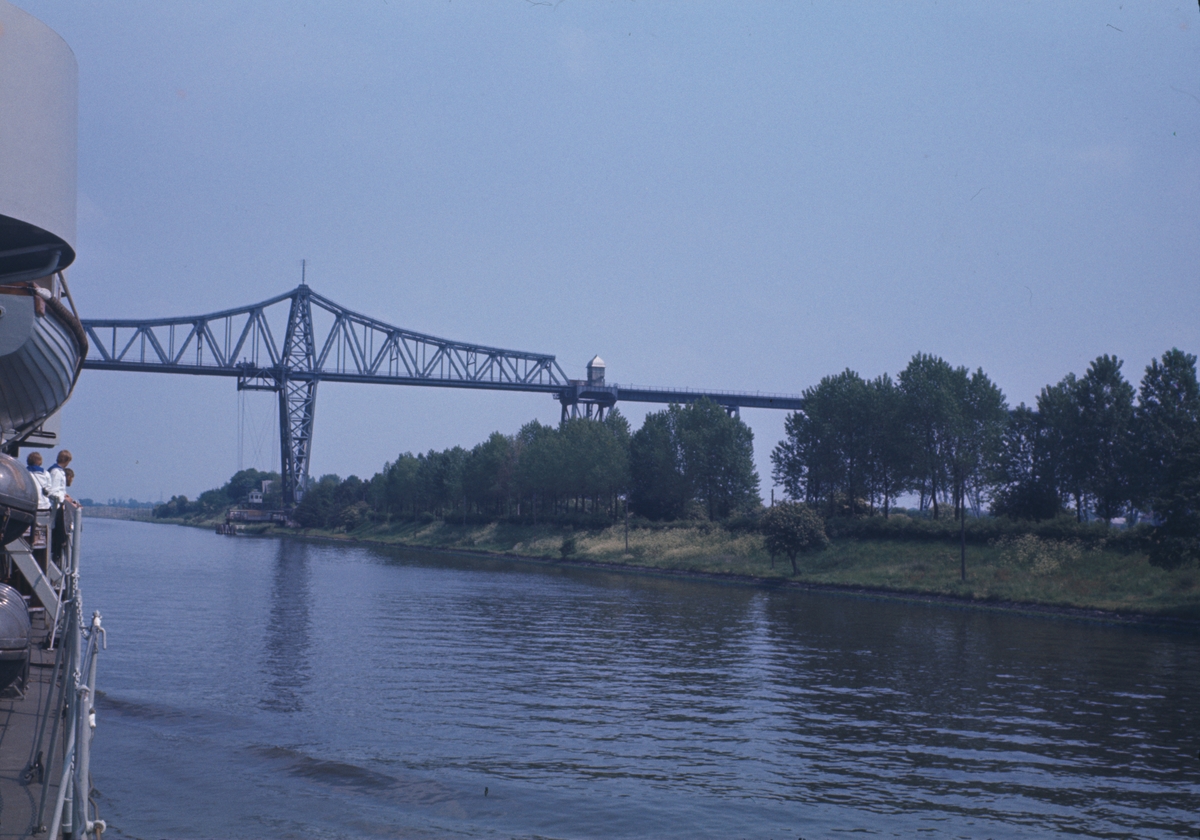 På bilden syns akterskeppet av jagaren Öland som precist har passerat järnvägsbron i Rendsburg. Under bron ser man den kända hängfärjan.