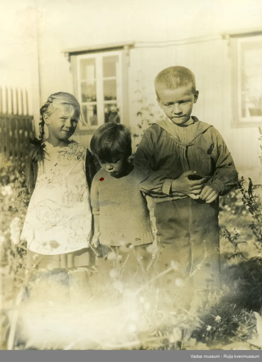 Barn foran trehus i sommersol.