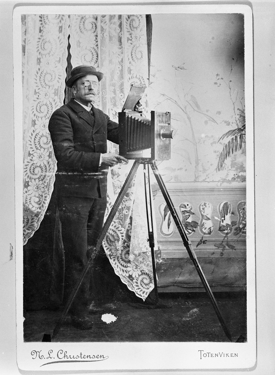 Sjølportrett av fotograf Nils Ludvig Christensen tatt i atelieret på Skramstad, Østre Toten. Atelieret var i enbygning som lå 400-500 meter fra garden.