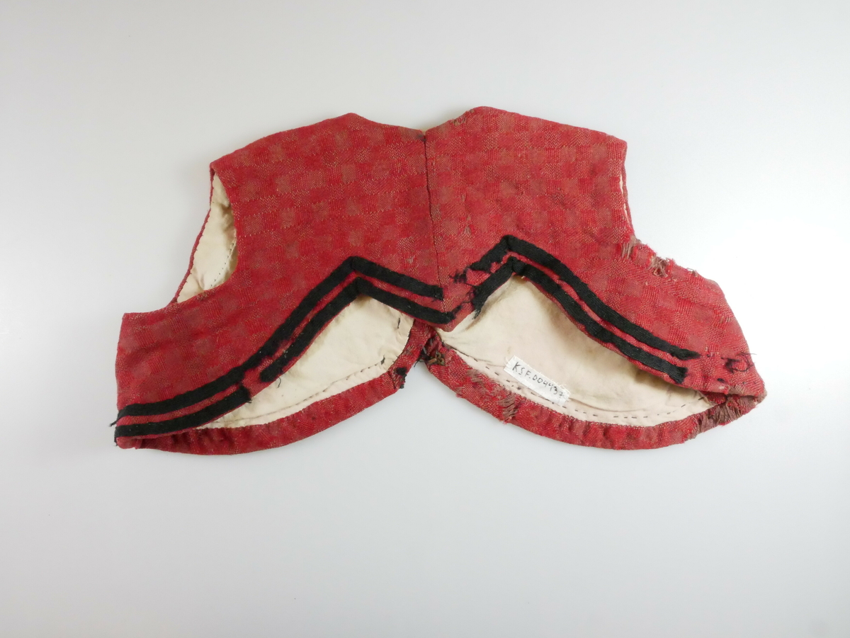 Rødt livstykke i ull med hvitt for. To svarte parallelle bånd nederst rundt livstykket. Tre metallhekter foran. 