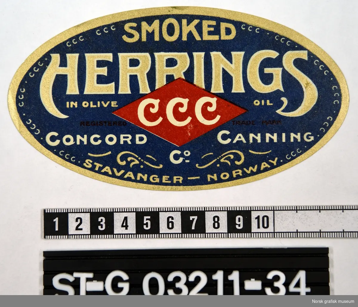 Oval etikett i blå, rød, hvit og gull.  

"Smoked Herrings in olive oil"