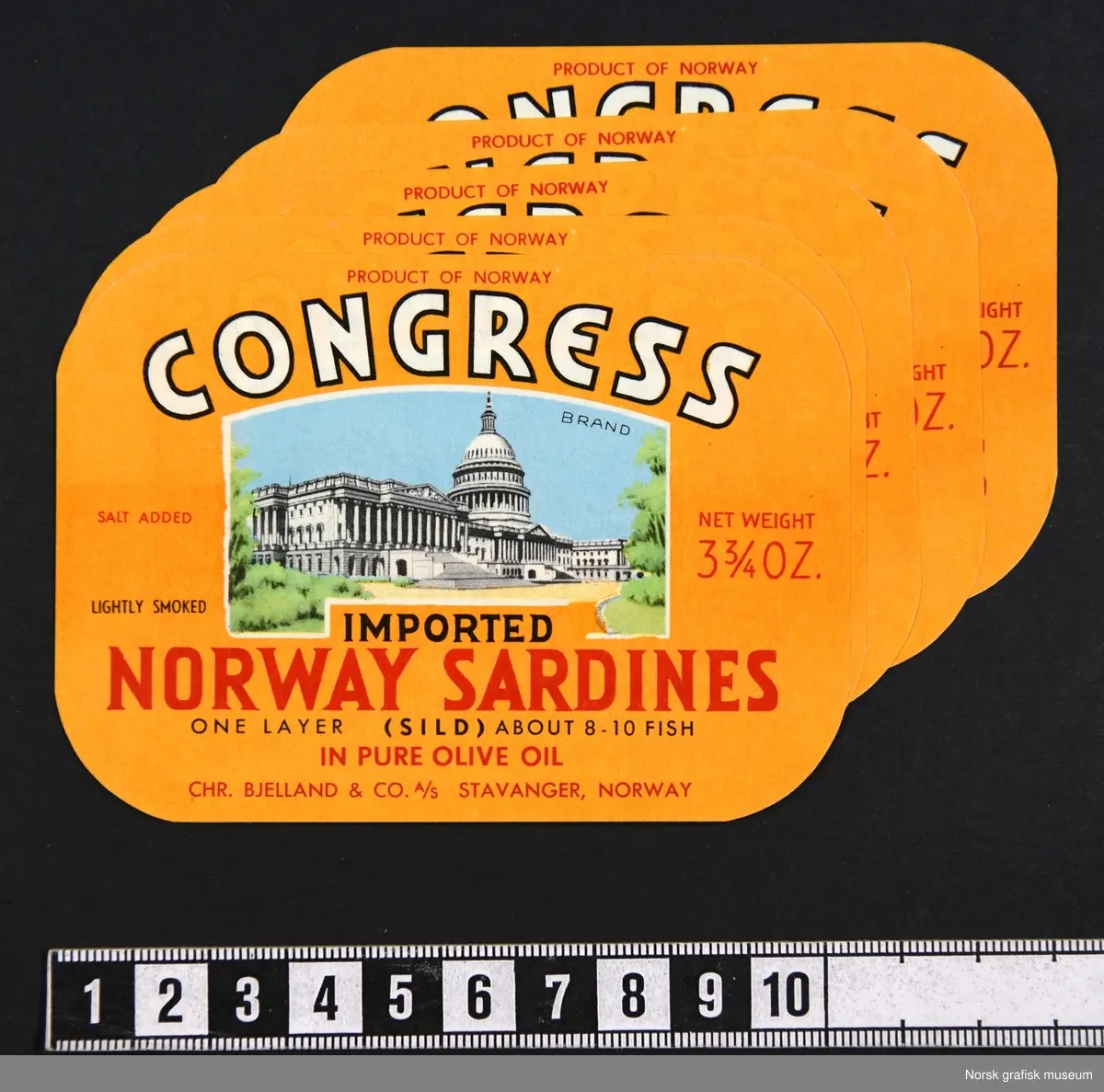 Etikett med oransje bakgrunnsfarge. Midt på etiketten er en fremstilling av United States Capitol, også kjent som Capitol building, Capitol bygningen, i Washington D.C.

"Imported Norway sardines in pure olive oil"