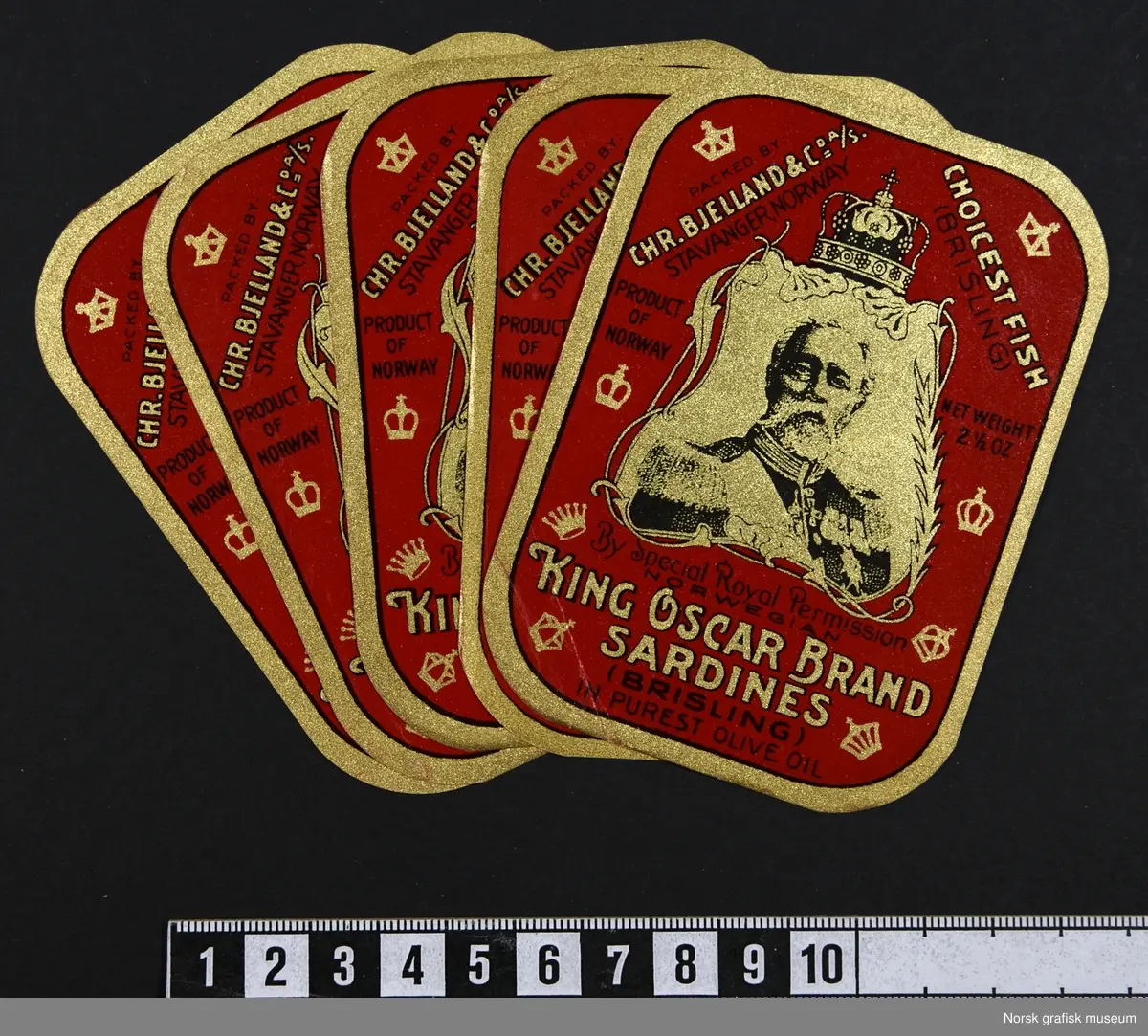 Røde etiketter med detaljer i gull og sort. Sentralt på etikettene er et portrett av Kong Oscar II en en dekorativ ramme rundt. 

"King Oscar brand sardines (brisling) in purest olive oil"