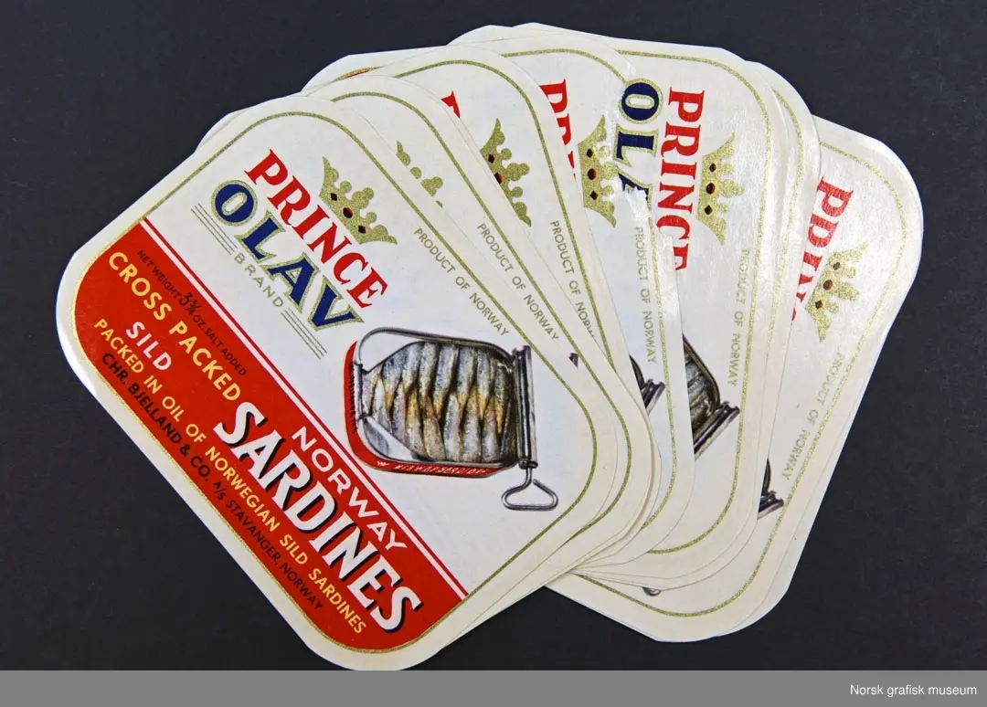 En bunke etiketter med hvit bakgrunn og røde detaljer. Ved siden av varemerket er en illustrasjon av en åpnet hermetikkboks. 

"Norway sild sardines packed in oil of Norwegian sild sardines."