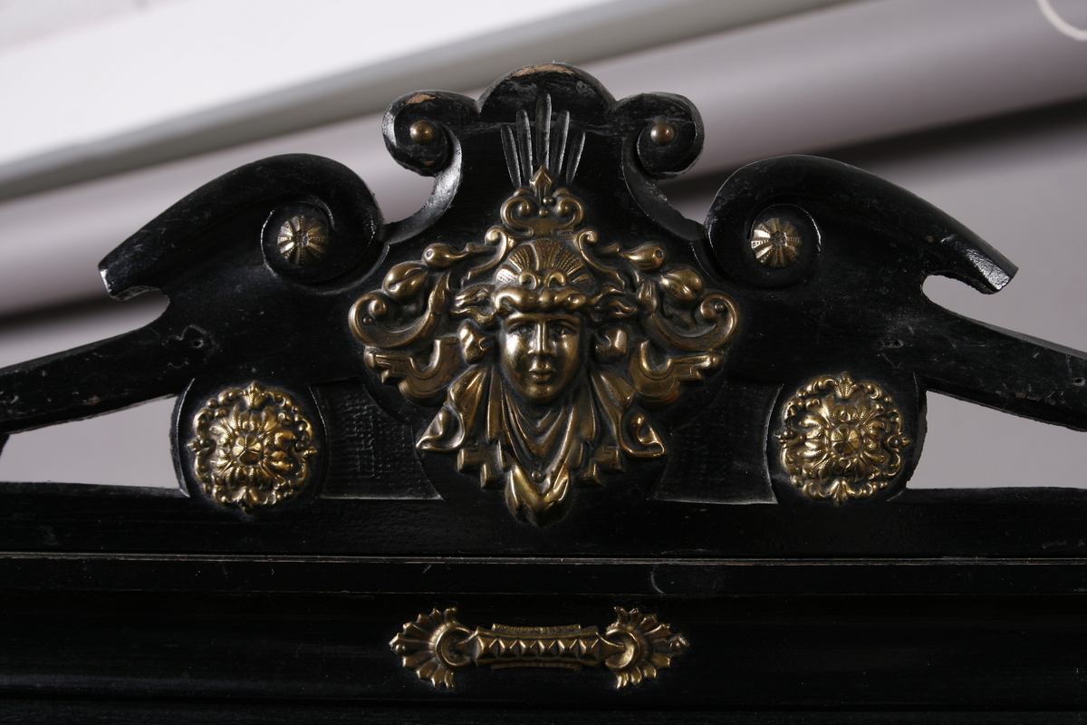 Notestativ i sortmalt tre. Notestol og fot kan settes sammen, foten deler seg i tre nederst. Rike profileringer på fot og stol, messingbeslag som er hamret i naturalistiske og stiliserte ornamenter. Stolen er på forsiden trukket med rustrødt, stoppet sikestoff. Denne kan reguleres på baksiden. Her kan men se merker etter to lister som sannsynligvis er det gamle festet mellom stol og fot.