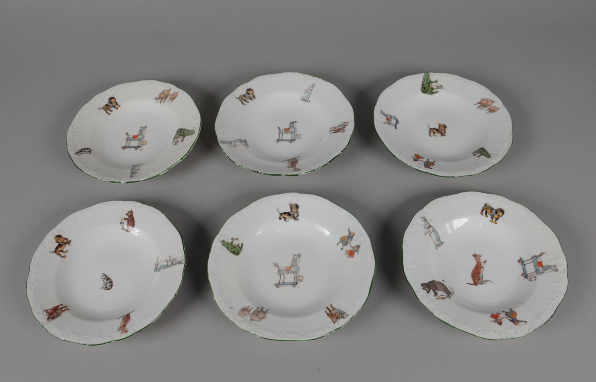 Seks leketallerkener av glassert keramikk. Randen er bølgete og har en dekorativ grønn stripe. Flerfarget trykk med motiv av dyr og leker, hver tallerken har forskjellige kombinasjoner av trykkene.