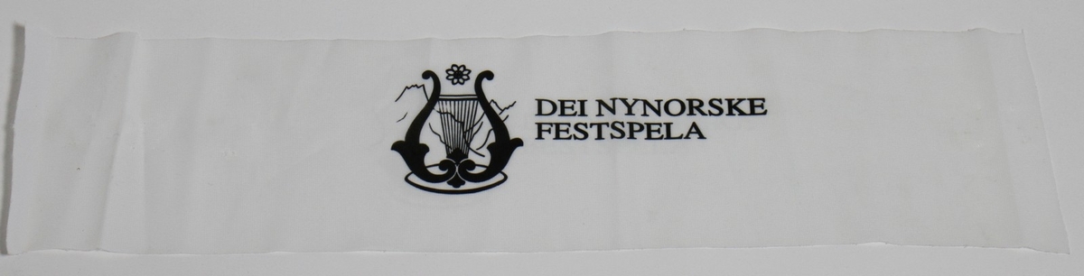 Kvitt tekstilband med svart tekst, som vart nytta under Dei Nynorske Festspela i 1994. Festspeldiktar dette året var Kjartan Fløgstad, og festivalen varde frå 9. til 18. september. Dei nynorske festspela er ein nasjonal festival som feirar den nynorske skriftkulturen, og festivalen vert arrangert årleg i Ørsta og Volda. (1) Det er uvisst kva bandet har vorte nytta til.

Kjelde:
https://www.allkunne.no/framside/tema-nynorsk/institusjonar-organisasjonar-med-meir/dei-nynorske-festspela/29/860/ (Lesedato: 07.08.2020)