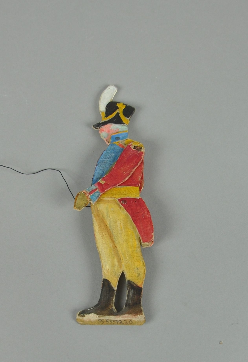 Figur av papp. Figuren forestiller en kaptein i sideprofil. Figuren har bevegelige armer, hode og overkropp, og er malt på begge sider.