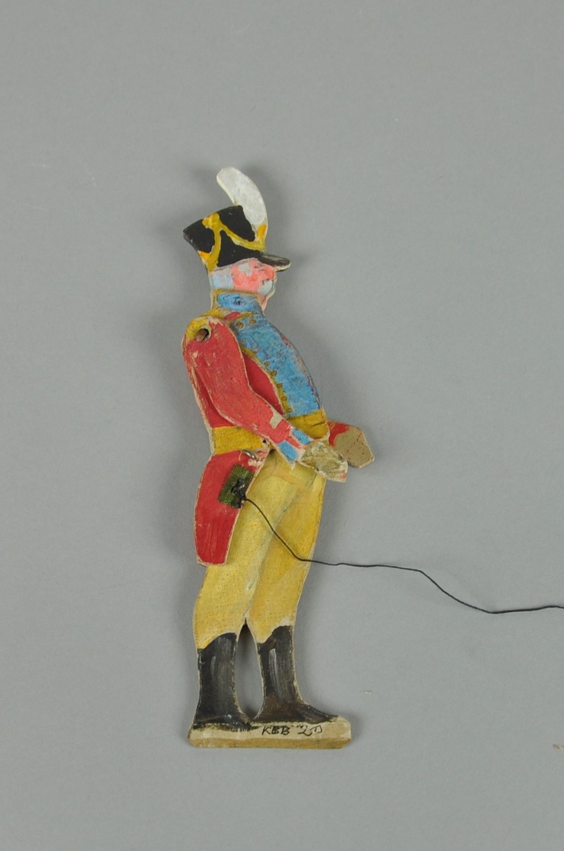 Figur av papp. Figuren forestiller en kaptein i sideprofil. Figuren har bevegelige armer, hode og overkropp, og er malt på begge sider.