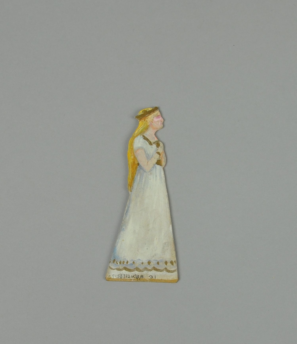 Figur av papp. Figuren forestiller dame i sideprofil, med hendene ved brystet. Figuren er malt på begge sider.