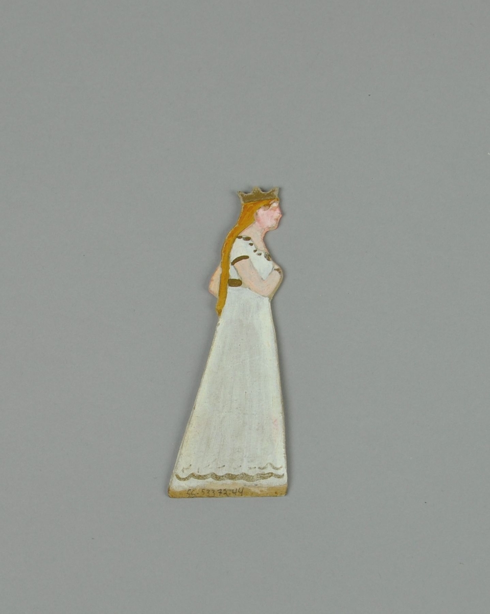 Figur av papp. Figuren forestiller stående dame i sideprofil, med krone og hvit kjole. Figuren er malt på begge sider.
