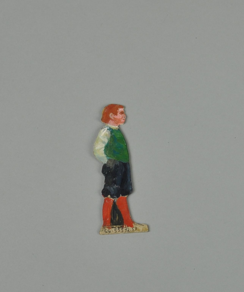 Figur av papp. Figuren forestiller gutt i sideprofil, med hendene i lommen. En annen del kan skyves over figuren, slik at gutten holder to bøtter. Figuren er malt på begge sider.