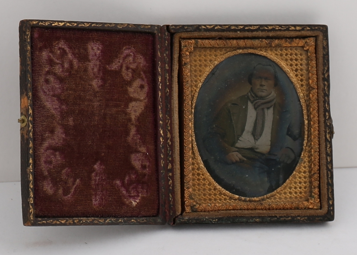 Daguerreotypi av mann som sitter ved et bord. Håndkolorerte hudtoner.