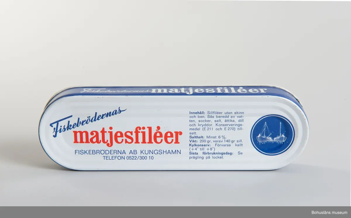 Avlång burk med rundade ändar. Tryckt dekor i blått, vitt och rött. 
Text: "Fiskebrödernas matjesfiléer. Fiskebröderna AB Kungshamn"
I bottnen innehållsförteckning.

Om givaren: Se UM026667.

Under slutet av 1800-talet byggde Kungshamnsskepparen  Hilmer Johansson tre små magasin på Fiskeskär intill sin kaj i Kungshamn. Här bedrev han under 1880-90-talet salteri, tunnbinderi och fraktfart. Bröderna Knut  och Manfred Kristiansson hyrde tillsammans med sin släkting Knut Hedberg ett av magasinsutrymmena på Fiskeskär av Hilmer Johanssons sterbhus och bildade 1920 bolaget Bröderna Kristiansson & Co, som senare blev känt för sina goda inläggningar under namnet Fiskebrödernas Konserver. 1942 bildades aktiebolaget Fiskebröderna AB och sortimentet utökades till hel- och halvkonserv i alla former. 1974 såldes rörelsen till Västkustfisk AB,  men behöll namnet Fiskebröderna AB. Västkustfisk AB  hade ett samarbete med Svenska Västkustfiskarnas Centralförbund SVC. Man fortsatte i oförminskad omfattning och flyttade 1987 rörelsen till Hovenäset och uppköptes av ABBA 1988.

Materialet är insamlat av Bohusläns museum i februari 1988 i samband med att konservfabrikens byggnader revs.

Se även tidigare inv.nr från Fiskebröderna AB: UM24171 - UM24185, UM24191, UM24192.

Material om konservindustrin i Bohuslän är arkiverad under Dokumentation-och Kulturminnesvårdsavdelningen med seriesignum M7D.
Se även tidningsartikel om sortimentet i Bilagepärmen, UM15081.

Litteratur: Bohusläns samhälls- och näringsliv. 4. Konservindustrin.  (1983)  Bohusläns museum, Etnologiska institutionen vid Göteborgs universitet, Landstinget i Göteborgs och Bohus län.
Kungshamn, Gravarne - Bäckevik och Fisketången genom seklerna. Arbetsgruppen för Kungshamnsboken. Uddevalla 1996.
Ur hav till burk och kartong. Fiskberedningen i Sotenäs kommun. Projekt Sverige i Blixtbelysning. Kungshamns Dokumentationsgrupp, Bohusläns museum 1996, se särskilt 
s. 16-17, 23-24