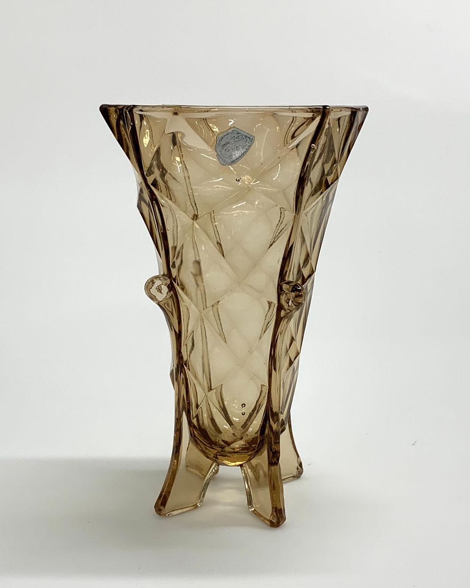 Pressad bruntonad vas, men facettimitationer och fyra eleganta fötter som sträcker sig uppåt vasens sidor och avslutas i finess.