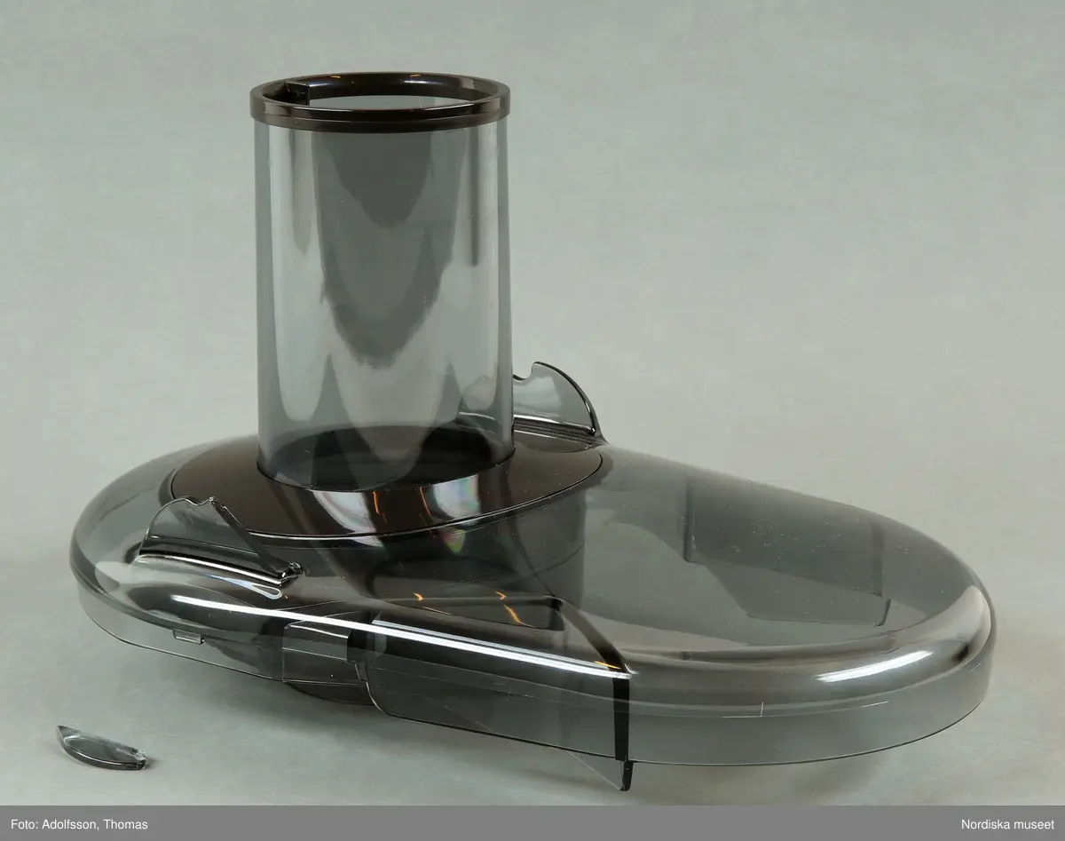 En elektrisk råsaftcentrifug av märket Elektrolux PERFECTJUICE ESF 2000. Består av  6 delar. a) Själva råsaftcentrifugen är cylinderformad och av metall och plast. De övriga delarna är av rökgrå hårdplast och består av b+) ett lock med c) press samt en d) behålllare som fruktköttet samlas i och e) en liten lockförsedd juicekanna med f) skumseparator i form av en plasskena som saften rinner ut i när den är klar. Dessutom en g) bruksanvisningsbroschyr och ett h) garantipapper.
Locket (b+) har en skada där en bit är avslagen.

Lena Kättström Höök 2014-01-10