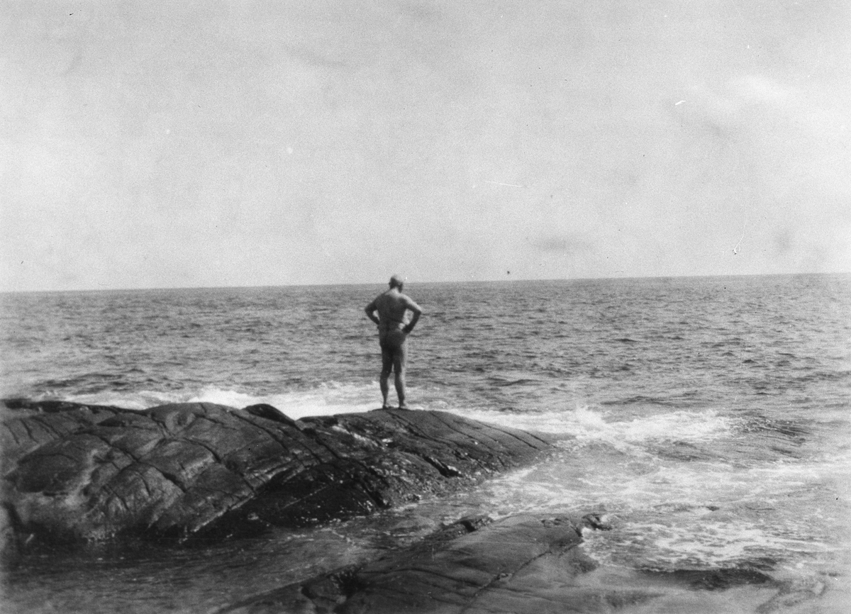 Mann står på et skjær ved havet. Fotografert 1925.