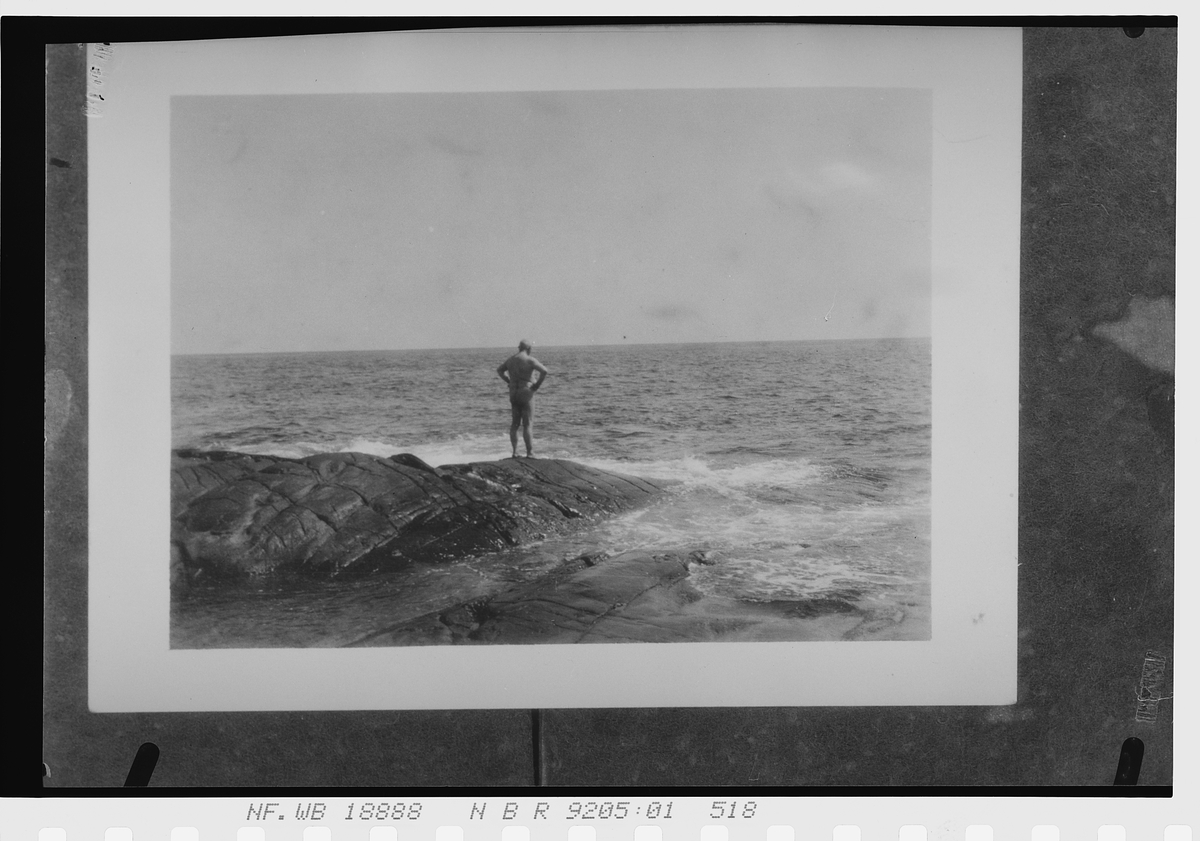 Mann står på et skjær ved havet. Fotografert 1925.