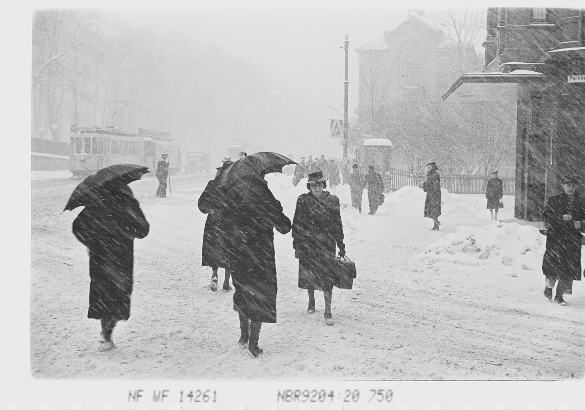 Personer med paraply i vintervær i krysset Drammensveien/Parkveien, Oslo. Fotografert 1941.