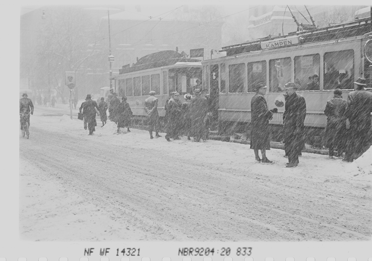 Personer i snøvær på trikkestopp ved Nobelinstituttet. Trikken til "Kampen", Henrik Ibsens gate, tidligere Drammensveien, Oslo. Fotografert 1941.