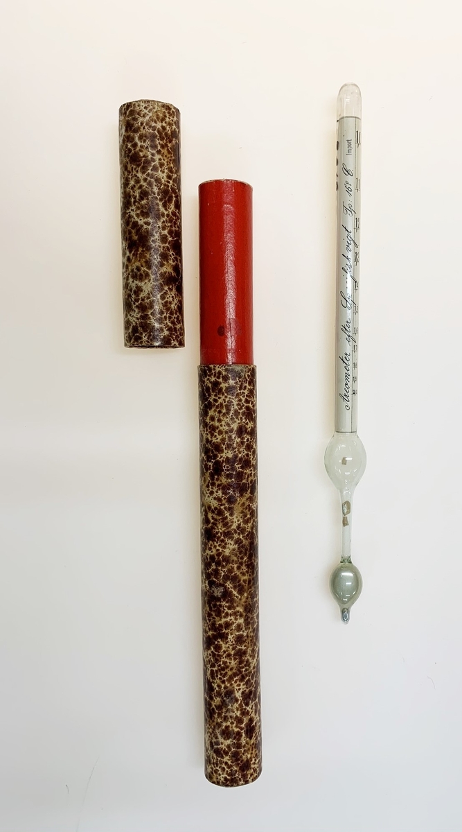 Areometer med tillhörande papprör, användes för att bestämma specifik vikt på vätskor. Påminner om en termometer. Nederst en uppblåst kula med flytande kvicksilver, vilken övergår i ett smalt rör som i sin tur övergår i ytterligare en (tom) kula. I "mätdelen" ett papper med skala och texten: "Areometer efter Specifisk vigt Tp: 15 C".