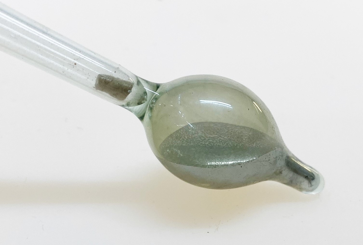 Areometer med tillhörande papprör, användes för att bestämma specifik vikt på vätskor. Påminner om en termometer. Nederst en uppblåst kula med flytande kvicksilver, vilken övergår i ett smalt rör som i sin tur övergår i ytterligare en (tom) kula. I "mätdelen" ett papper med skala och texten: "Areometer efter Specifisk vigt Tp: 15 C".