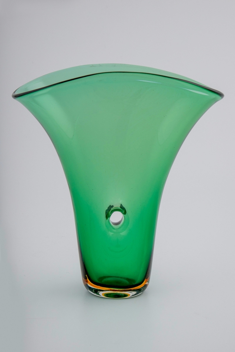 Grønnfarget vase i gjennomskinnelig glass. Vasen hviler på en ovalformet bunn, som er utført i gulbrunt og klart glass i overfangsteknikk. Fra den smale bunnen reiser vasens vegger seg i en bred vifteform, hvor langsidene er forbundet med et gjennomgående hull i midten. Ujevn ovalformet munningsrand.