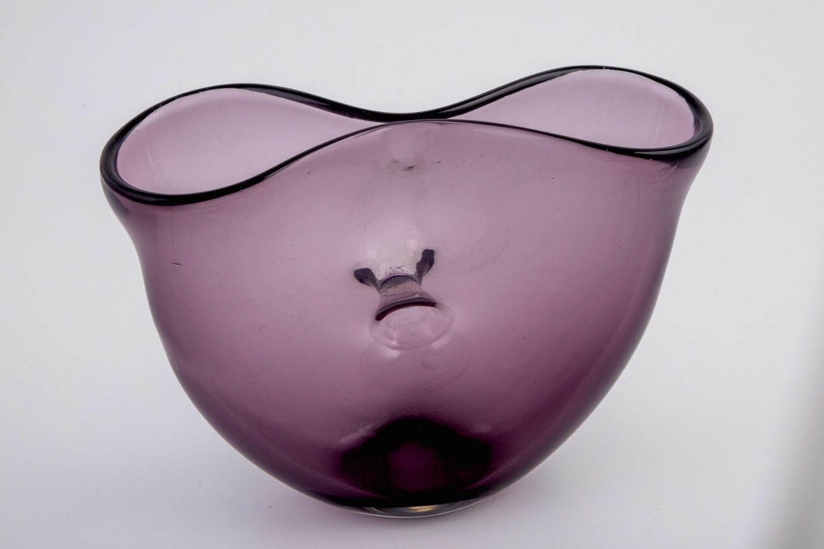 Vase i gjennomskinnelig lillafarget glass. Ovalt korpus med et gjennomgående hull i midten. Vasens munning har form av et åttetall, hvor kantene nesten møtes på midten.