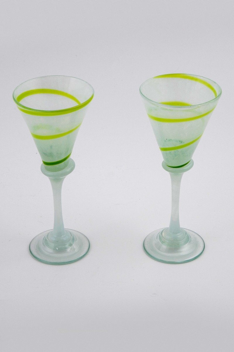 To glass i halvgjennomskinnelig glass. Kupa er melkehvit og dekorert med en grønn spirallinje. Overgangen til den melkehvite stetten er markert med en skjev vulst. Fotplaten er utført i klart glass.