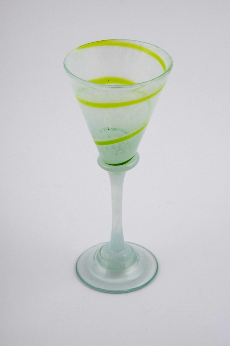 Drikkeglass i halvgjennomskinnelig glass. Kupa er melkehvit og dekorert med en grønn spirallinje. Overgangen til den melkehvite stetten er markert med en skjev vulst. Fotplaten er utført i klart glass.