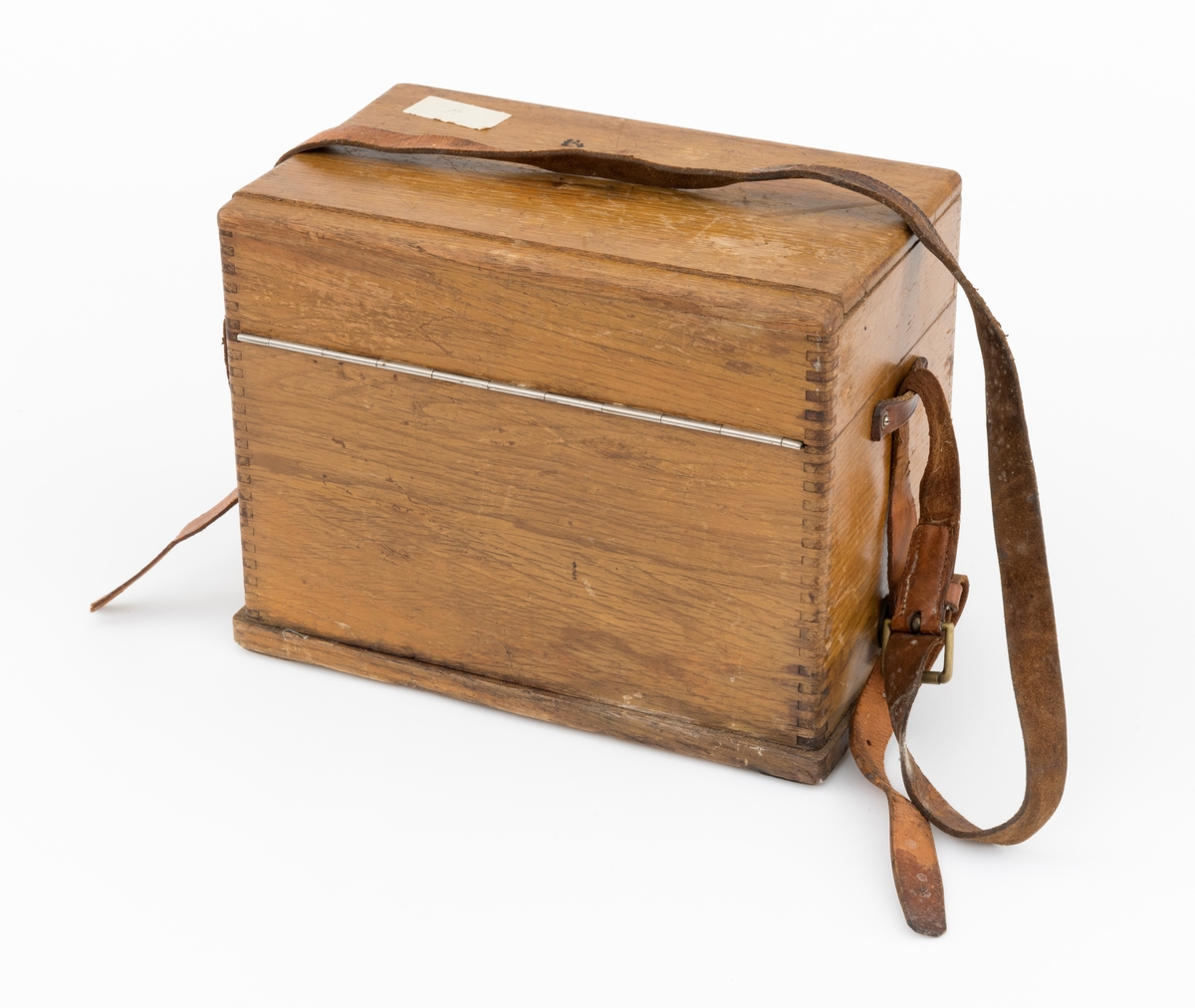 Bærbar felttelefon, antakelig av type som ble brukt tidlig på 1900-tallet. Telefonen er montert i ei trekasse, antakelig lagd av eikematerialer. Kassa har ei botnplate som er 33,1 centimeter lang, 20,2 centimeter bred og 1,5 centimeter tjukk. Ved endene av botnplatas underside er det 19,3 centimeter lange og 3,1 centimeter brede trelister som  gjenstanden sto på. Oppå den nevnte botnplata er det ei 32 centimeter lang, 19 centimeter bred og 16,6 centimeter høy kasse med fingerskjøtte, noe avrundete hjørner. Til denne kassas bakre langside er det hengslet et lokk av samme type materiale og med samme lengde og bredde som kassa. Lokket er 6,1 centimeter høyt. Lokket stenges ved hjelp av dreibare kroker på kassas frontside som vendes, slik at de omslutter skruer på lokkets frontside. Litt lengre neden på kassefronten er det et gjennombrutt hull med 1,3 centimeters diameter, antakelig innføringspunktet for sveiva til telefonen. Dette hukket kan stenges ved hjelp av ei lita, dreibar stålskive når sveiva ikke er i bruk. Da festes sveiva i en trekloss som er innlimt i et hjørne i lokket. Telefonen bæres i ei cirka 2,4 centimeter bred lysebrun lærrein, som er festet i messingknapper, sentralt på den nedre delen av kassas tverrender. At kassa bæres med den riktige sida opp er sikret ved hjelp av smøyestoler av lær høyere oppe på de samme endeflatene. Lengden på bærereima kan justeres ved hjelp av ei nålespenne. Inne i kassa er det antakelig et batteri, skjult under trelokk i to plan. På det nedre er det inntappet en toleddet, forkrommet holder for telefonrøret. Også telefonrøret er forkrommet, med har bakelittkomponenter for håndgrep (midten), øreanlegg og taletrakt. Sentralt på lokkets underside er det pålimt en trekloss med et tjukt svart filtbelegg, som skulle holde telefonrøret på plass under transport. Ellers er det innlimt to etiketter på undersida av lokket. Den ene er et firmamerke som refererer til «AKTIESELSKABET ELEKTISK BUREAU, KRISTIANIA, NORGE». På dette merket er det et rødt skjold med en løvefigur med krone over. Undersida av lokket er det også påklistrert en etikett med tekniske spesifikasjoner fra produsenten. Denne kontrollseddelen har også vært nummert, datert og signert, men hjørnet hvor blant annet årstallet har stått, er dessverre avrevet.
