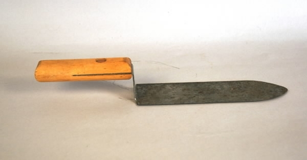 Avtäckningskniv, av trä och metall. Innan honungen slungas måste cellockenavlägsnas. Cellocken som består av vax avlägsnas med en avtäckningskniv.Kniven består av ett träskaft ur vilket metallbladet böjs två gånger i räta vinklar, och avslutas med en bredbladig metallklinga med avrundad spets.Klingan har slipad egg och handtaget är fastsatt med en kopparnit.