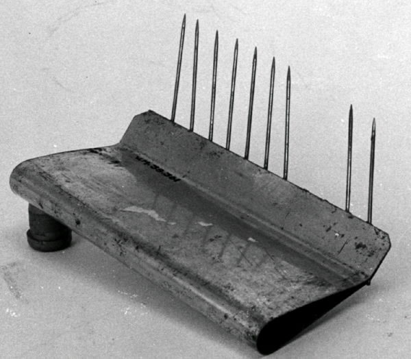 Kakstöd av metall, som används som stöd vid perforering av sega kakor med cellperforator. Hopvikt metallskiva som avslutas i ett veck i vilket vassa metallnålar är fastsatta. Saknas: tre nålar.