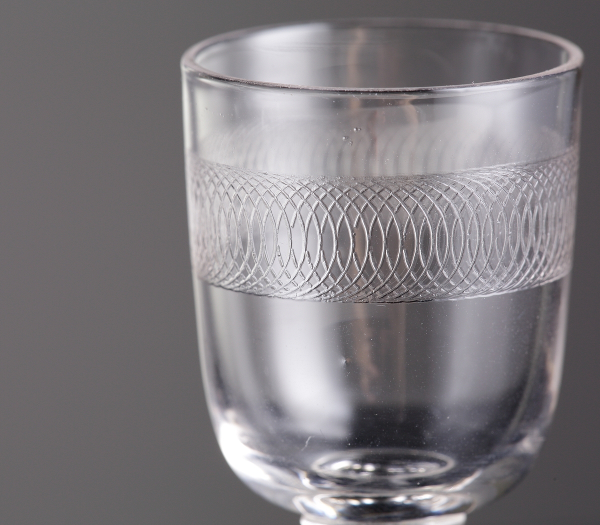 Glas (R.275).
Beskrivning: Guillocherad eller pantograferad bård.
Färg: Ofärgat klarglas.
Mått: Diameter ovan avser glasets fotdiameter.
Inskrivet i huvudkatalogen 1942.
Funktion: Servisglas