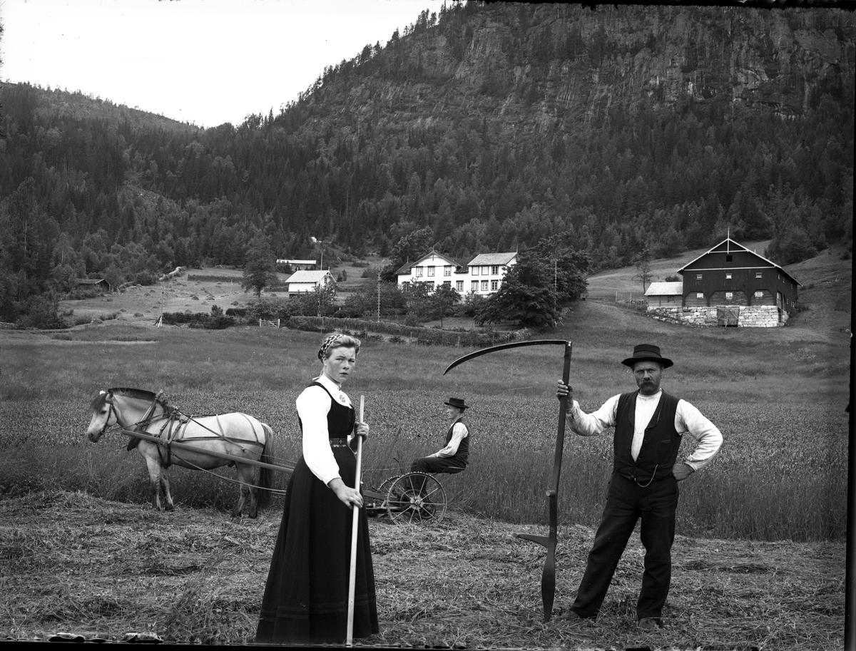 Fotosamling etter Bendik Ketilson Taraldlien (1863-1951) Fyresdal. Gårdbruker, fotograf og skogbruksmann. Fotosamlingen etter fotograf Taraldlien dokumenterer områdene Fyresdal og omegn. 
Portrett av Åse Modøl med rive, M. Bergland med ljå, og Jørund Lauland sitter på slåmaskinen fra kornslåtten på Taraldlien.