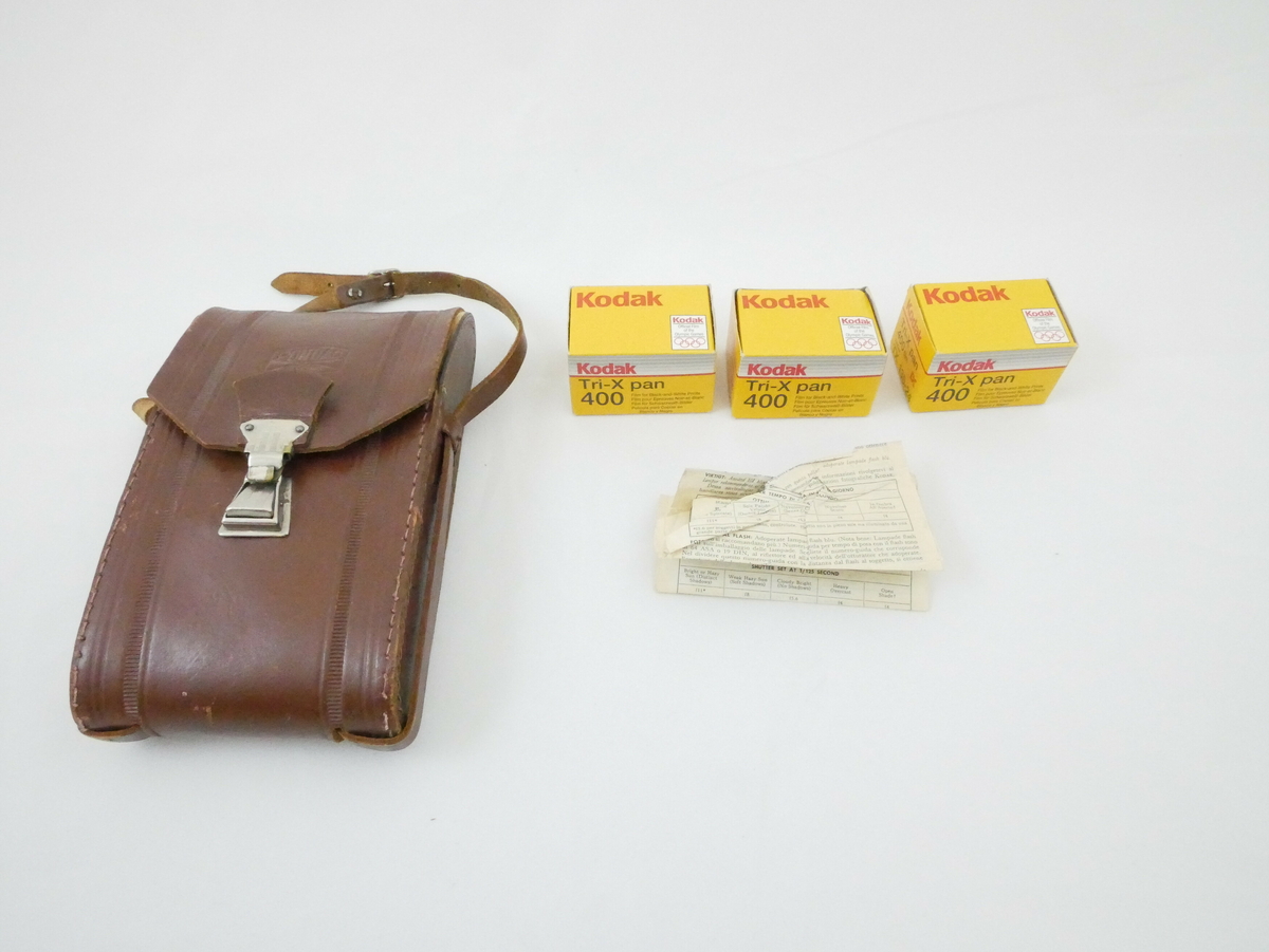 Mørkebrun oval veske i skinn eller lær. Vesken har et bøyd lokk øverst som festet med en metallfeste i enden. Ett bånd i samme materiale som vesken er festet på begge sider, båndet har hakk og en metallfeste til å stramme med. Inne i vesken er det tre gule kartongemballasjer for filmrull, og en bruksanvisning på hvitt papir. 

Påskrift på veske: 
PONTIAC // PARIS
MADE IN PARIS

Påskrift på emballasje: 
KODAK // Tri- X pan // 400