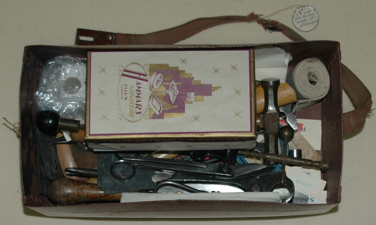 Verktygsväska, unikabox, medförd av Hedvig Ulfsparre då hon hängde utställningar. Väskan innehåller ett antal verktyg samt en ask med etiketter, spik m.m. På asken står texten "Hammars konditori , Falun, Telefon 24" tryckt.