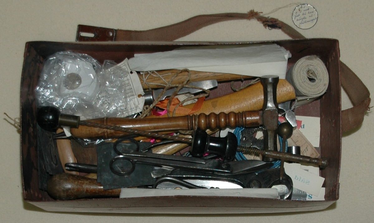 Verktygsväska, unikabox, medförd av Hedvig Ulfsparre då hon hängde utställningar. Väskan innehåller ett antal verktyg samt en ask med etiketter, spik m.m. På asken står texten "Hammars konditori , Falun, Telefon 24" tryckt.