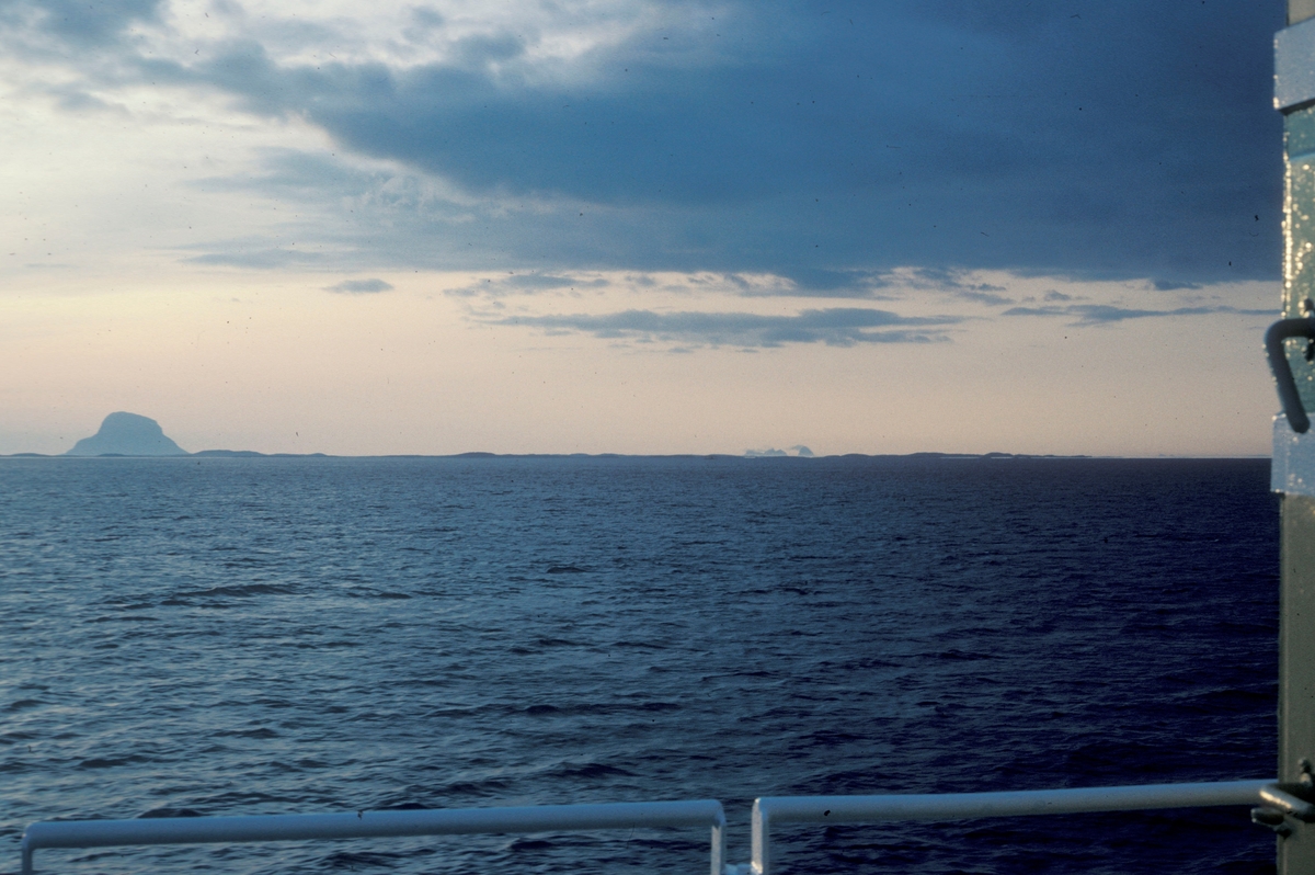 Fotografi tatt fra en båt. Utsikt utover havet med øyene Lovund og Træna i bakgrunnen.