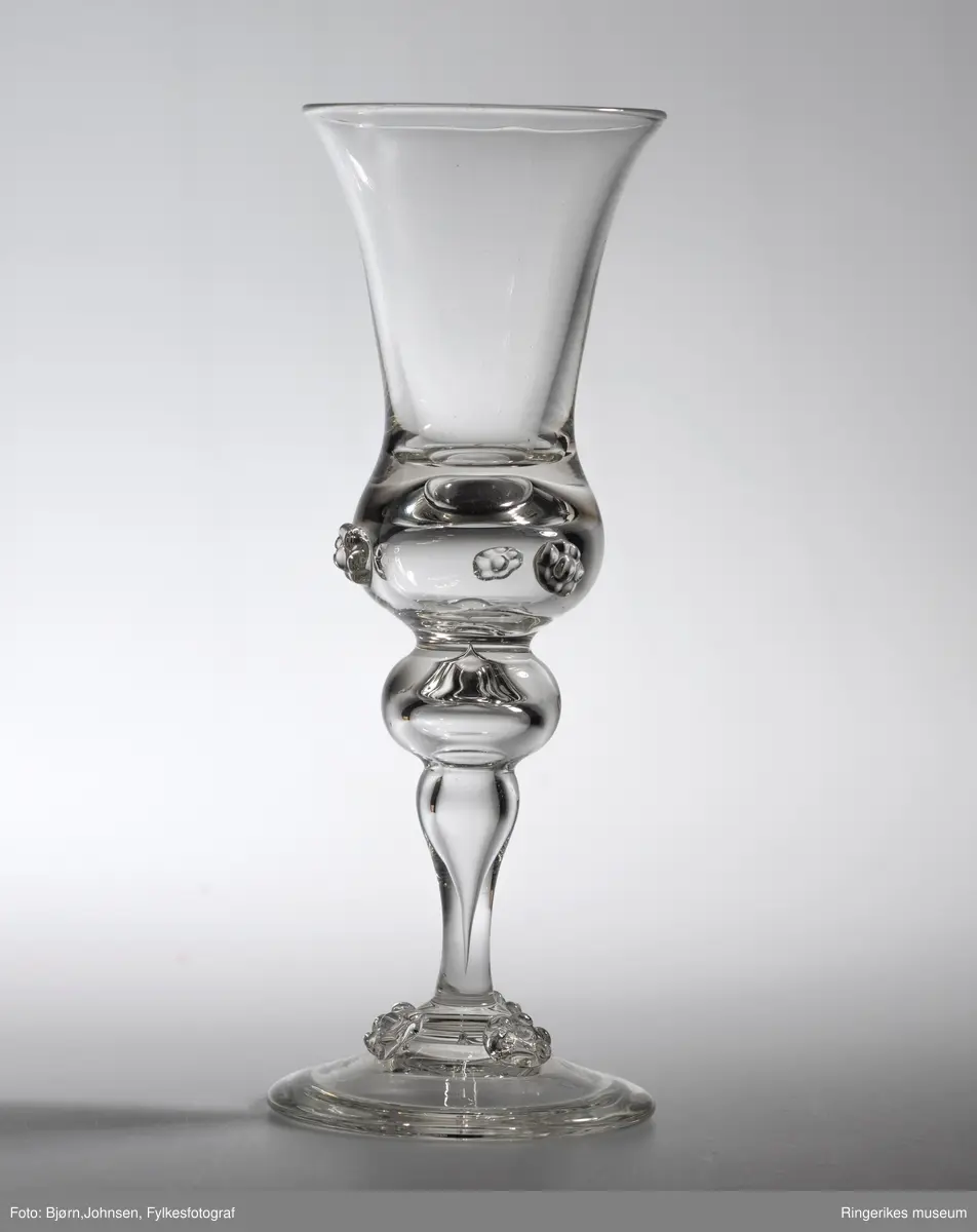 Klukk drammeglass med bringebærornamenter på både glass og stett. Fra serien Nøstetangen, produsert fra 1876 på Hadeland Glassverk.